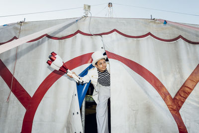 Male juggler holding juggling pins standing with stilts in circus tent