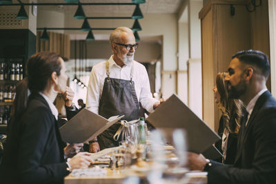 Waiter talking to business people while standing by table in restaurant