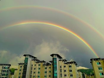 Low angle view of rainbow over buildings in city against sky