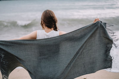 Rear view of woman sitting on beach against sky