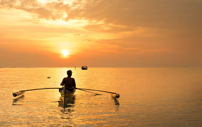 Silhouette man in sea against sky during sunset