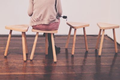 Low section of woman sitting on stool against wall