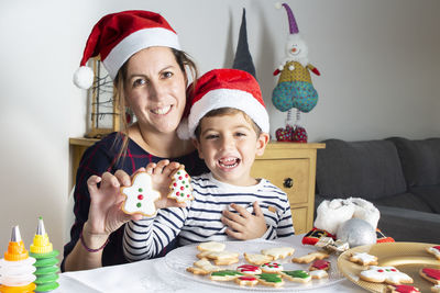 Portrait of happy boy and mother holding gingerbread cookies at home