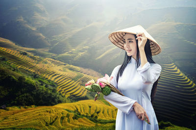 Beautiful young woman holding flowers while standing on mountain