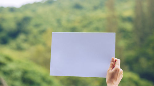 Cropped image of hand holding paper against blurred background