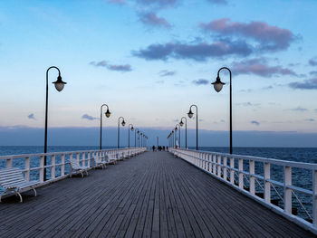 Street lights on pier by sea against sky