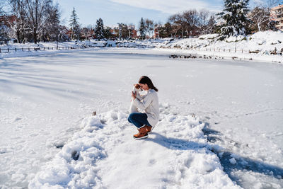 Woman hugging cute jack russell dog while standing on snowy pier by frozen lake during winter