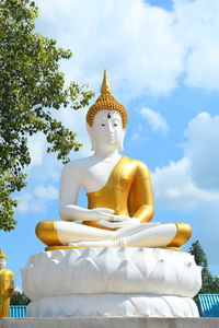 Low angle view of gold buddha statue at temple against sky