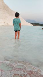 Rear view of boy standing at beach against sky