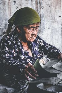 Senior woman with leaves sitting against wooden wall