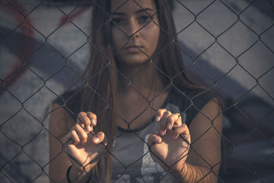 Portrait of woman looking through chainlink fence