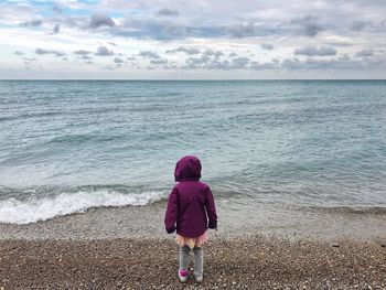 Rear view of girl standing on sea shore at beach against sky