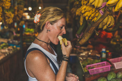 Side view of mature woman eating banana at market during night