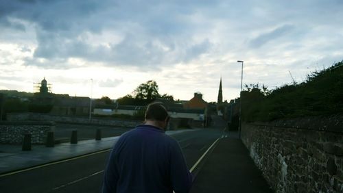 Rear view of man with arms raised against cloudy sky