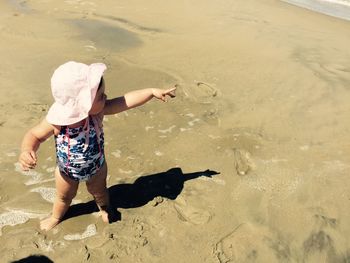 Full length of cute baby girl pointing while standing on shore at beach during summer