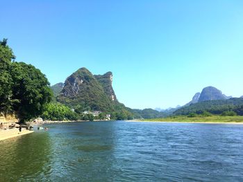 Scenic view of sea and mountains against clear blue sky