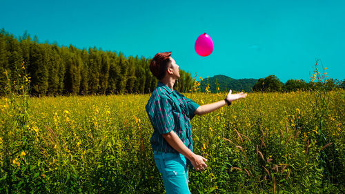 Side view of young man playing with balloon on land during sunny day
