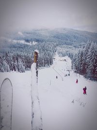 People skiing on snow covered field against sky