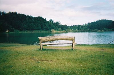 Empty bench by lake against sky