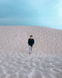 Man walking on sand dune at desert against cloudy sky