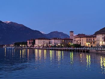 Illuminated buildings by lake against blue sky at dusk