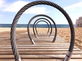 Metal railing on beach against sky