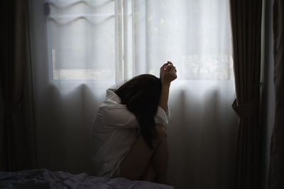 Side view of depressed woman sitting by window at home