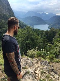 Man looking at river and mountains against cloudy sky