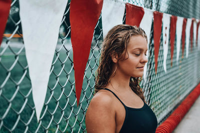 Young woman in swimwear by chainlink fence