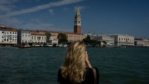 Rear view of woman by buildings against sky in city