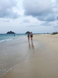 Sisters walking at beach against sky