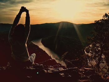 Rear view of woman with arms raised against sky during sunset