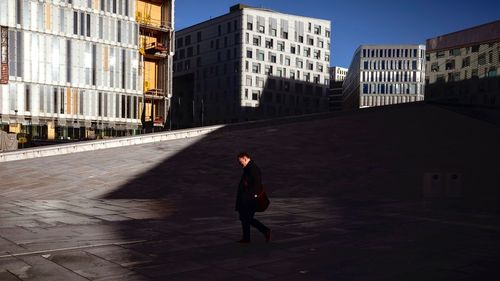 Full length of woman standing on footpath amidst buildings in city