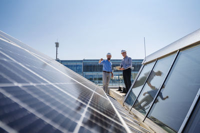 Two executives in hardhats discussing on the rooftop of a solar-powered company building