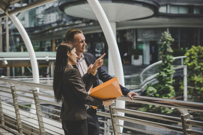 Colleagues discussing file while standing on footbridge