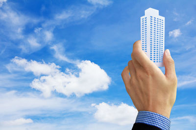 Cropped of business person holding model building against cloudy sky