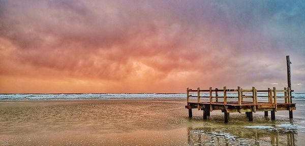 Pier on beach against sky during sunset