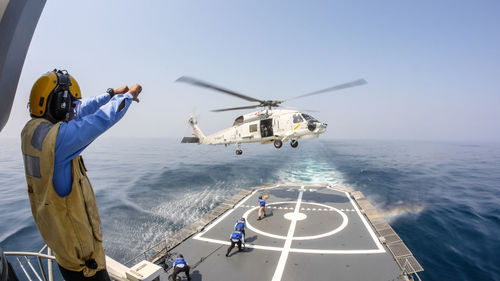 Rear view of helicopter flying over sea against sky