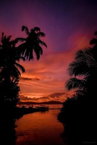 Silhouette palm trees by sea against romantic sky at sunset