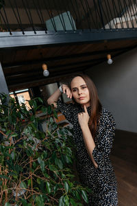 A woman in a dress with polka dots stands next to a green interior bush