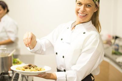 Portrait of happy female chef garnishing pasta in plate at commercial kitchen