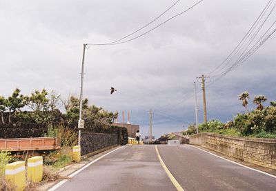 Road by electricity pylons against sky