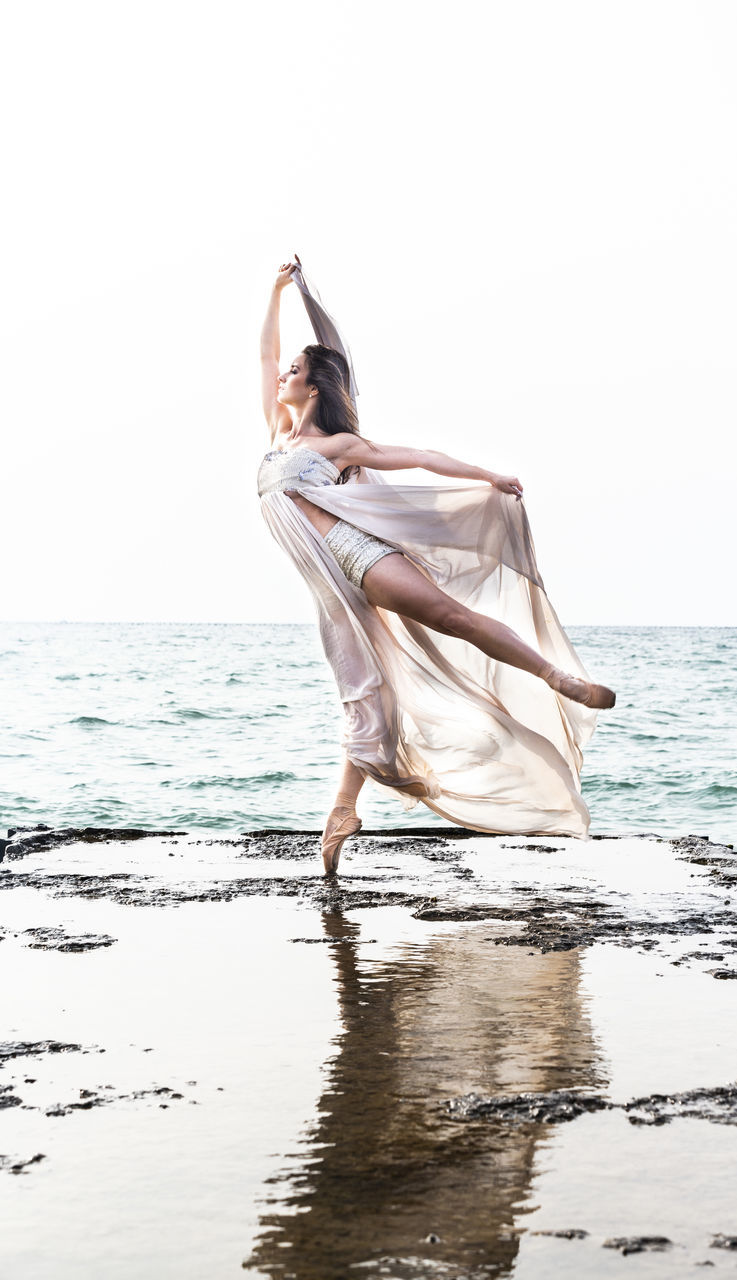 sea, water, one person, real people, young adult, full length, beach, sky, beauty in nature, women, leisure activity, motion, adult, nature, young women, dancing, land, lifestyles, horizon over water, outdoors, human arm, arms raised, beautiful woman