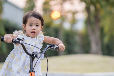 Yellow dressed beautiful little girl riding bicycle at park.