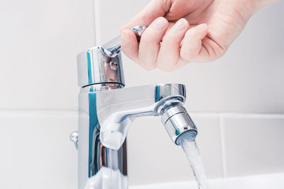 Close-up of person using faucet in bathroom