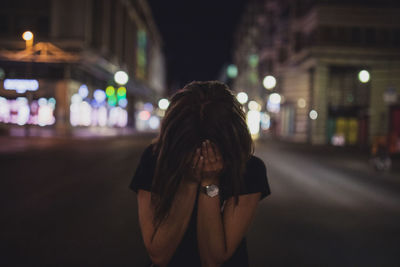 Terrified woman covering face while standing on street at night