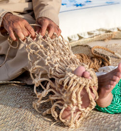 Old man is knitting traditional fishing net, hands and feet in frame