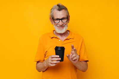 Senior man holding coffee cup against yellow background