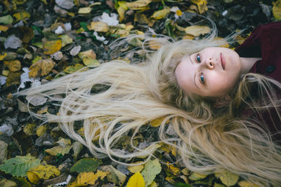 High angle portrait of young woman lying on leaves covered field during autumn