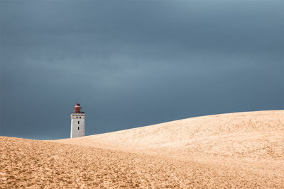 Lighthouse on beach by building against sky